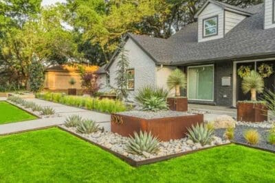 Modern front yard landscape in Russwood Acres Dallas, TX with Corten steel edging, agave, river rock, ornamental grasses, and concrete walkway