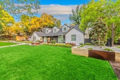 Wide front yard landscape in Russwood Acres Dallas, TX with green lawn, Corten steel planters, river rock beds, agave, and mature trees
