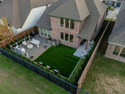 Aerial view of a fenced backyard in University Place Dallas, TX with artificial turf lawn, deck seating, and border shrubs