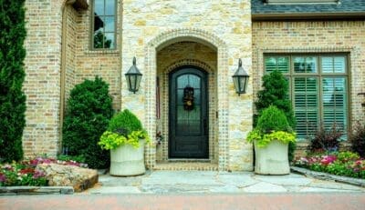 Close-up front entry landscape design in North Dallas, TX with decorative pots, evergreen shrubs, seasonal flowers, stone walkway, boulder accent, and exterior lighting.