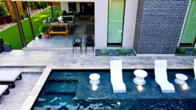 Luxury backyard pool with in-water loungers, custom hardscape, and covered patio in a Dallas, Texas outdoor living project