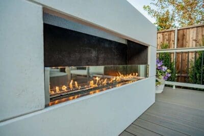 Close-up of a modern white outdoor fireplace with linear flames on a composite deck in University Place Dallas, TX