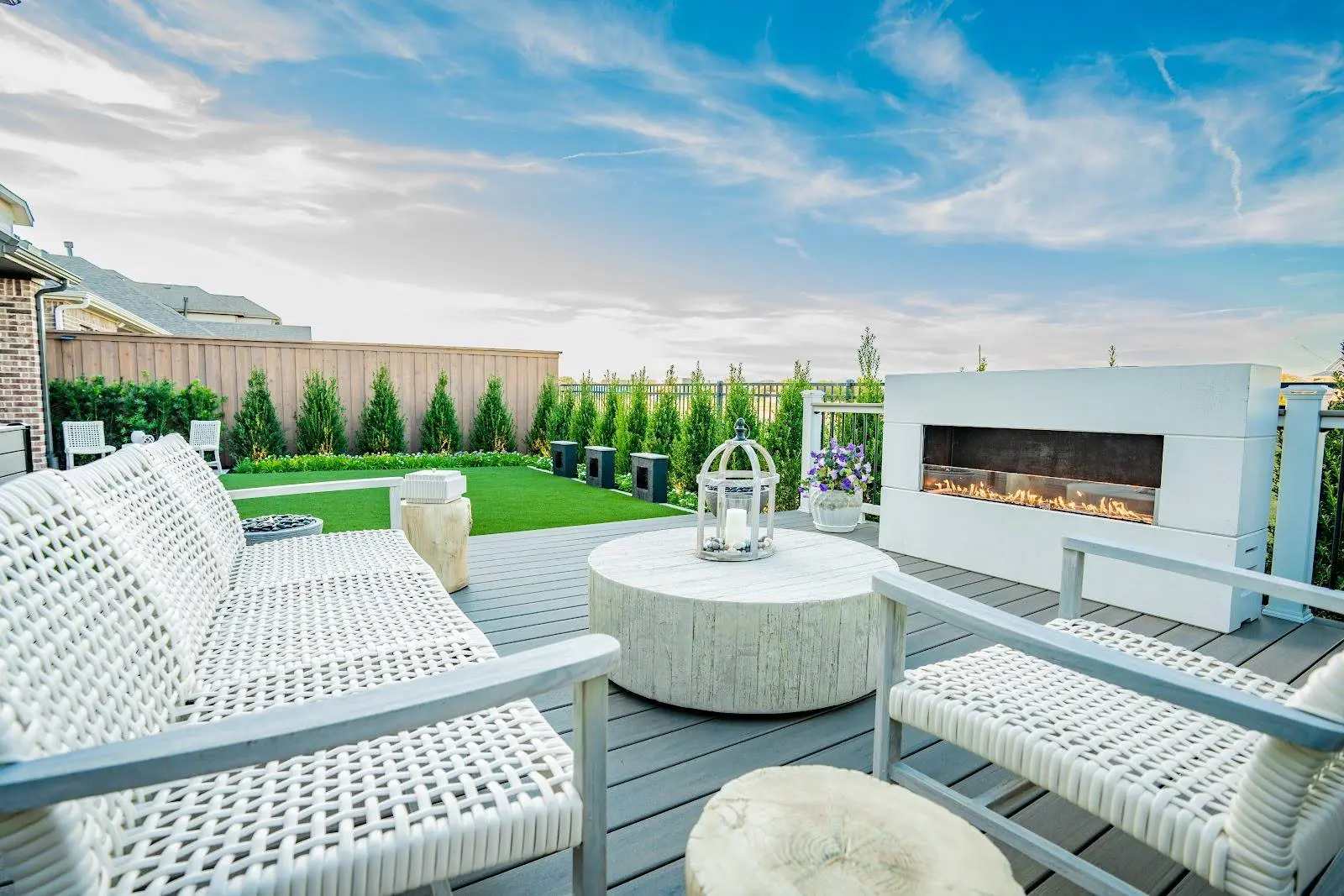 White outdoor seating on a composite deck in University Place Dallas, TX with a round coffee table, modern fireplace, and privacy plantings