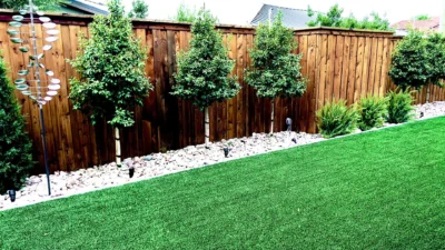Backyard privacy landscaping with ornamental trees, decorative rock border, and artificial turf installation in Dallas, Texas