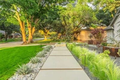 Modern concrete walkway in Russwood Acres Dallas, TX with ornamental grasses, agave, river rock, black gravel, lawn, and low path lighting