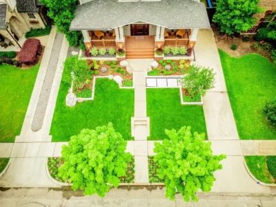 Aerial view of front yard landscape design in Lakewood Dallas with concrete walkway, green lawn, defined planting beds, boulder accents, and mature street trees.