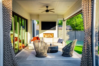 Covered outdoor living patio with lounge seating, fireplace, ceiling fan, turf lawn, and backyard sport court in Midway Hollow Dallas, Texas.
