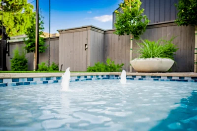 Modern backyard pool with bubblers, blue tile, privacy fence, planter, and soft perimeter landscaping in Midway Hollow Dallas, Texas.