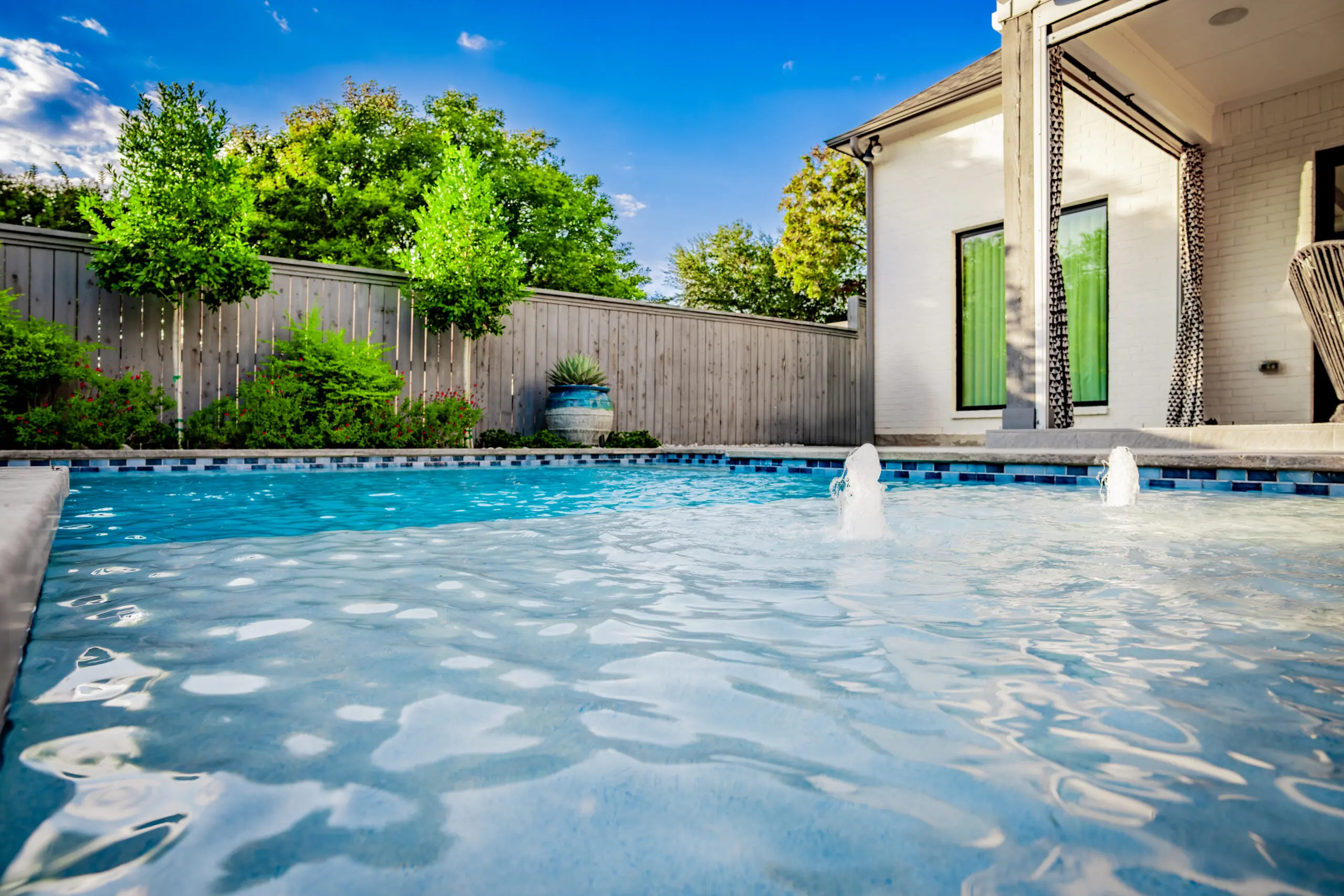 Modern backyard pool with bubblers, covered patio, privacy planting, and clean landscape design in Midway Hollow Dallas, Texas.