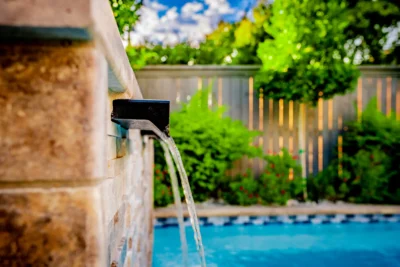 Close-up of modern pool water feature with stone wall, blue pool water, and soft privacy planting in Midway Hollow Dallas, Texas.