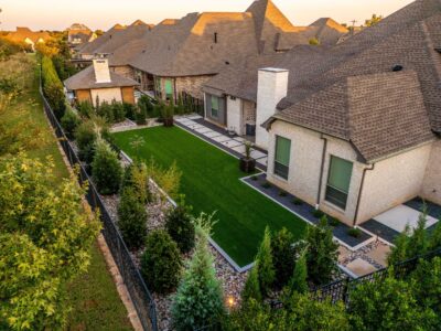 Aerial view of a Hidden Knoll backyard in Southlake, Texas, with artificial turf, stone walkways, river rock beds, privacy shrubs, and modern planter accents