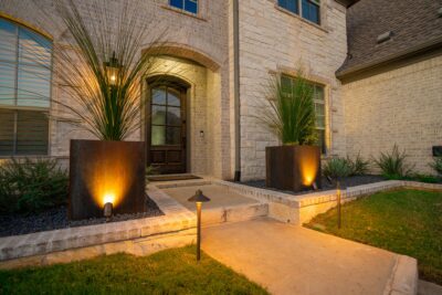 Front entry in Hidden Knoll, Southlake, Texas, with illuminated metal planters, pathway lights, agave, dark gravel beds, and stone steps