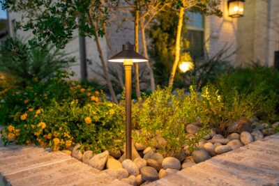 Close-up of a path light in a Southlake, Texas planting bed with river rock, lantana, shrubs, and warm outdoor lighting