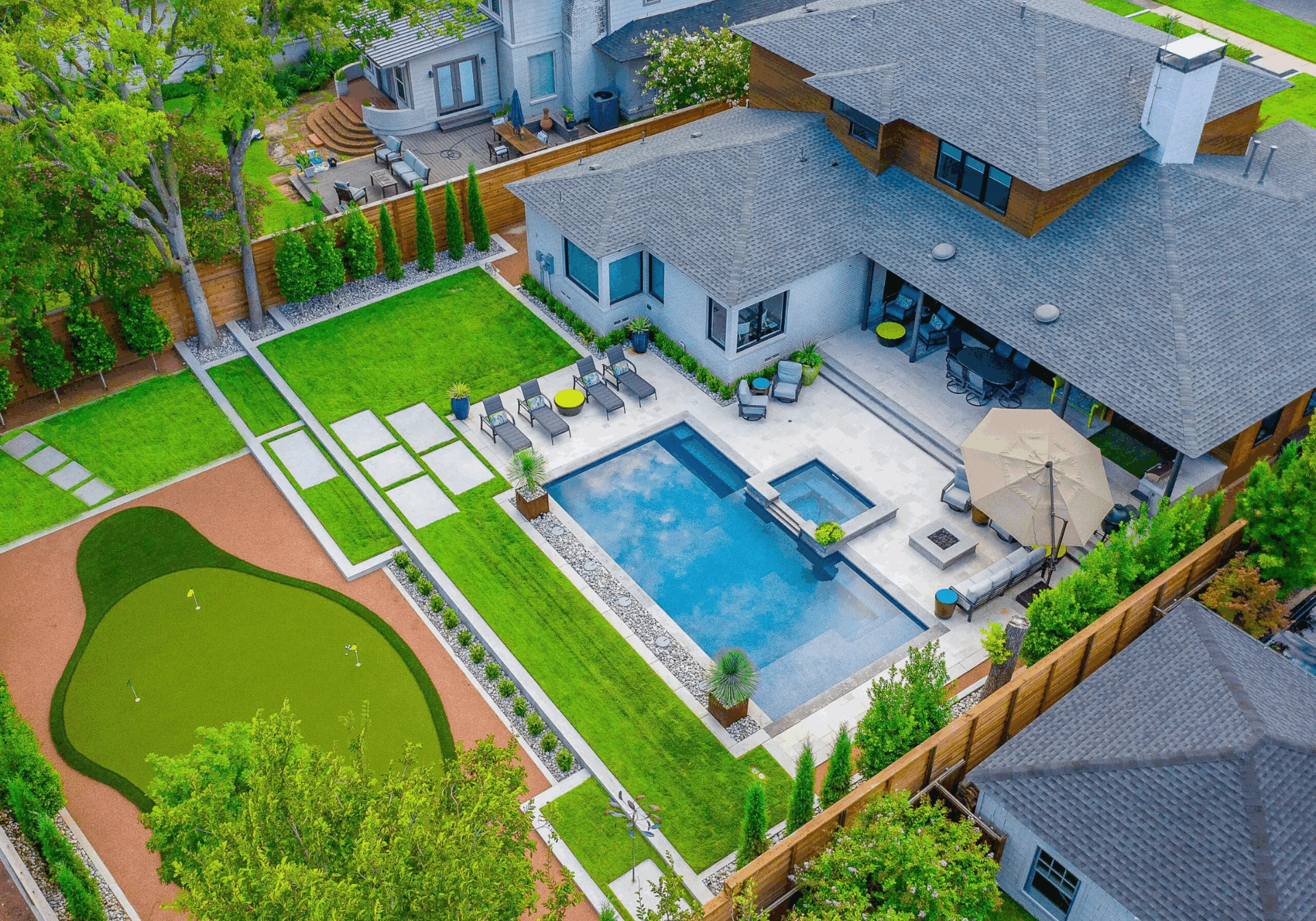 Aerial view of a modern backyard landscape design featuring a pool, patio seating area, manicured lawn, and private putting green at a Dallas, TX home.